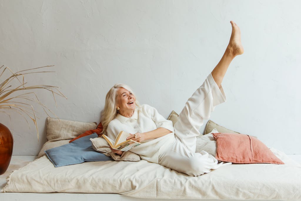 Joyful elderly woman relaxing indoors with a book, expressing carefree happiness.