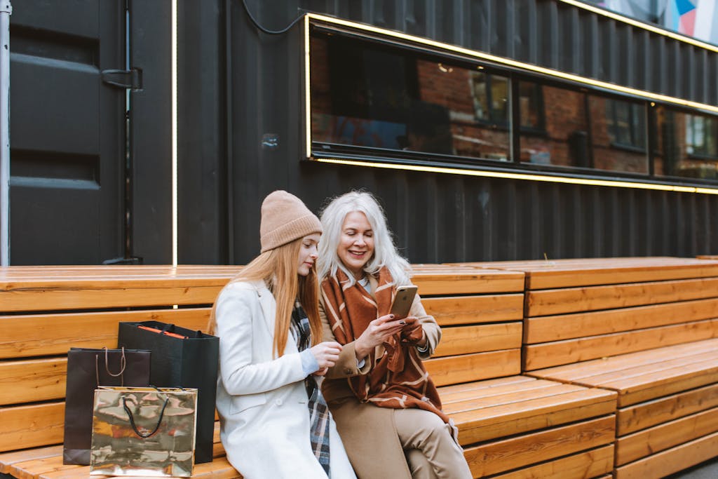 Elderly woman with teenage girl enjoying shopping day outdoors, bonding over smartphone.