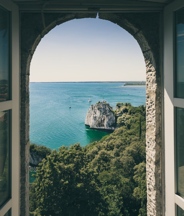 Idyllic view of Duino Cliffs and sea through arched window in Italy, perfect for travel inspiration.